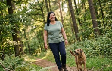 KI-generiert: Eine Frau spaziert mit ihrem Hund durch den Wald