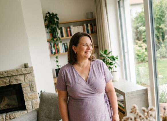 KI-generiert: Frau steht im Wohnzimmer und lächelt