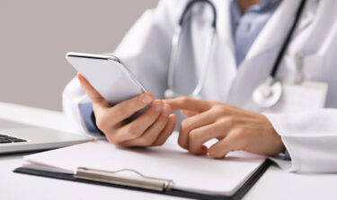 Arzt schaut auf sein Handy am Arbeitsplatz