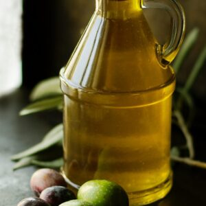 Glasflasche mit Olivenöl und Oliven davor