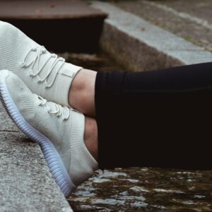 Auschnitt von Waden und Füßen einer Frau mit Sneakern, die auf einer Mauer abgelegt sind.