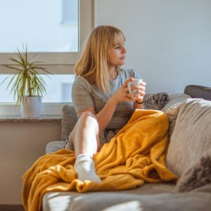 Frau sitzt auf einem Sofa und schaut zur Seite, über ihr liegt eine gelbe Decke.