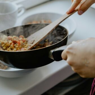 Eine Pfanne mit gekochten Gemüse wird über einen Teller gehalten, um das Essen darauf zu tun.