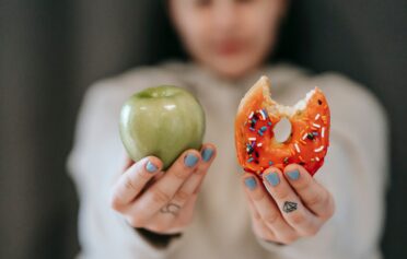 Frau hält einen Apfel und Donut