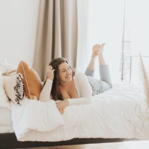 Frau mit lockigen Haaren liegt auf einem weißen Bett