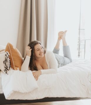 Frau mit lockigen Haaren liegt auf einem weißen Bett
