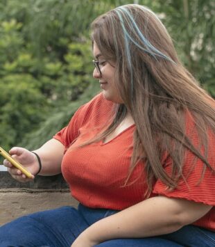 Frau sitzt auf einer Mauer und guckt auf Smartphone