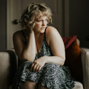 Plus size Frau sitzt nachdenklich auf einem Sessel.