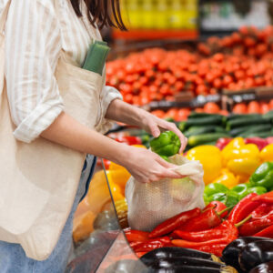 Frau mit Beutel steht im Supermarkt am Gemüse und kauft ein