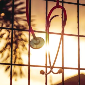 Ein Stethoskop hängt vor einer Fensterscheibe im Sonnenuntergang.