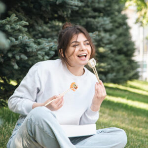 Junge Frau sitzt im Park und isst glücklich ein Stück Sushi