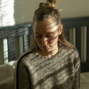 Frau mit halb offenen Haaren sitzt auf einem Bett und guckt nach unten