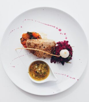 Weißer Teller mit einem kunstvoll angerichteten Fleischgericht. Es ist eine kleine Portion.