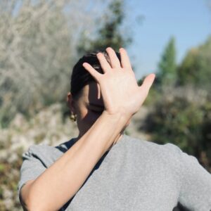 Eine Frau steht in der Sonne und hält sich die Hand vor ihr Gesicht um Schatten zu spendne.