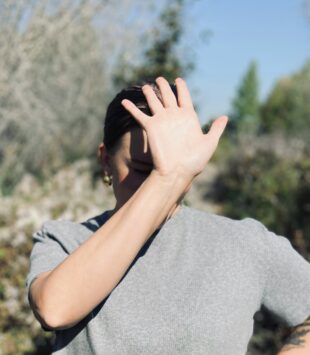 Eine Frau steht in der Sonne und hält sich die Hand vor ihr Gesicht um Schatten zu spendne.
