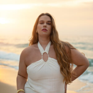 Eine selbstbewusste Frau in einem weißen Sommerkleid posiert am Strand.