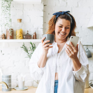 Junge, glückliche Frau mit Handy in der Küche