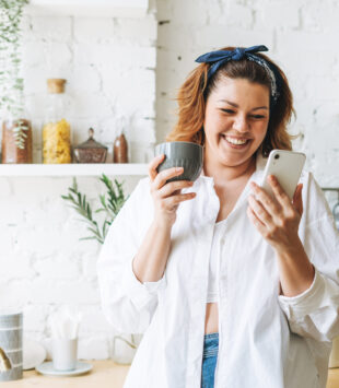 Junge, glückliche Frau mit Handy in der Küche
