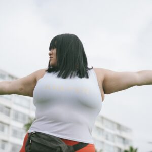 Eine plus size Frau bei Sport streckt beide Arme von sich weg und blickt über den linken Arm.