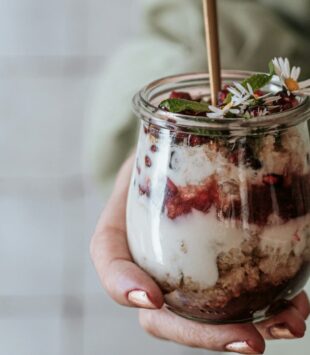 Frau hält ein Glas mit geschichtetem Chia Pudding und Früchten in der Hand