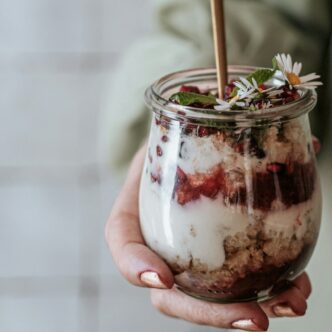 Frau hält ein Glas mit geschichtetem Chia Pudding und Früchten in der Hand