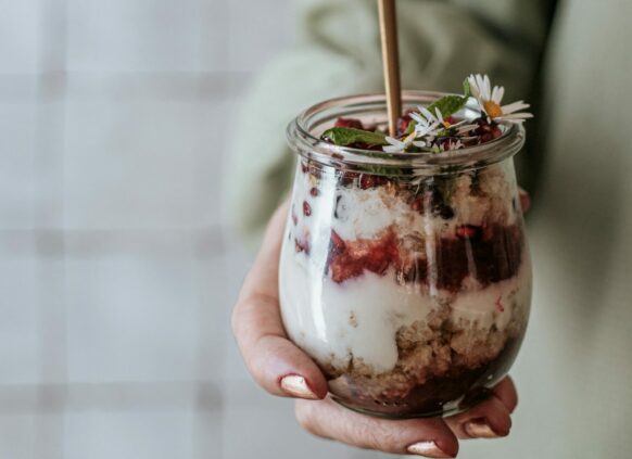 Frau hält ein Glas mit geschichtetem Chia Pudding und Früchten in der Hand