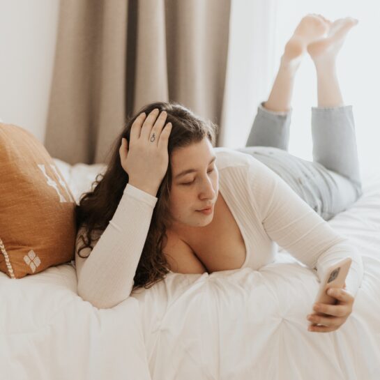 Frau liegt auf dem Bett und schaut sich etwas auf ihrem Smartphone an.