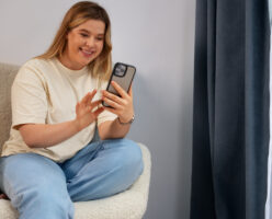 Eine junge Frau sitzt auf in einem Sessel und scrollt fröhlich auf ihrem Smartphone.