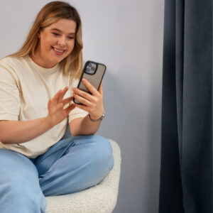 Eine junge Frau sitzt auf in einem Sessel und scrollt fröhlich auf ihrem Smartphone.