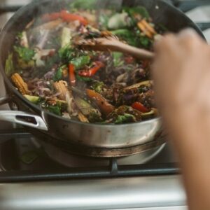 Eine Pfanne mit buntem Gemüse steht auf dem Herd und wird umgerührt.