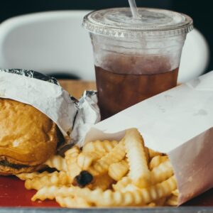 Eine Platte mit ungesundem Essen, wie Pommes, Burger und Cola.