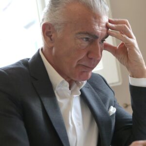 Ein älterer Herr im Anzug sitzt am Schreibtisch und hält sich den Kopf.