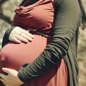 Frau mit grün roter Kleidung hält Babybauch