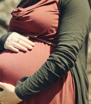 Frau mit grün roter Kleidung hält Babybauch