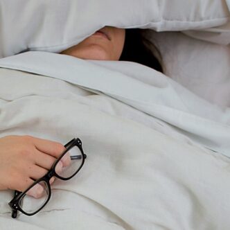 Frau liegt erschöpft im Bett mit Brille in der Hand