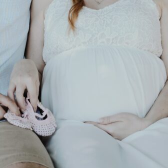 Frau im weißen Kleid hält rosa Babyschuhe