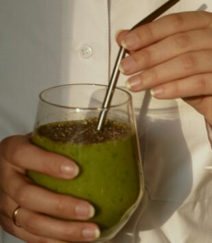 Frau in weißer Bluse hält ein Glas mit einem grünen Smoothie