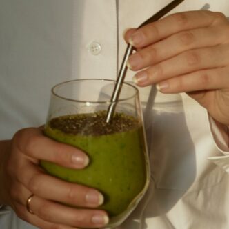 Frau in weißer Bluse hält ein Glas mit einem grünen Smoothie