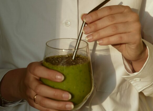 Frau in weißer Bluse hält ein Glas mit einem grünen Smoothie