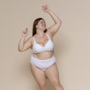 plus size Frau tanzt in Unterwaesche vor einem beigen Hintergrund
