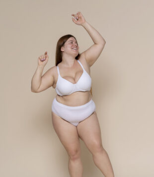 plus size Frau tanzt in Unterwaesche vor einem beigen Hintergrund