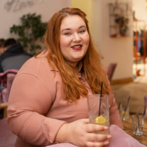 Laxhende übergewichtige Frau hält ein Glas in der Hand.