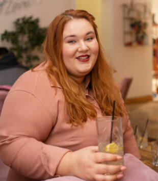 Laxhende übergewichtige Frau hält ein Glas in der Hand.