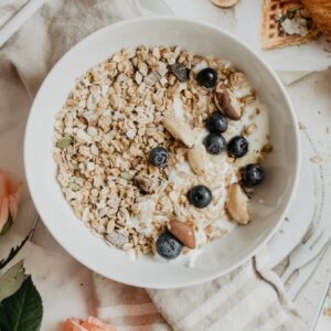 Schale gefüllt mit Müsli mit Leinsaamen, Obst und Joghurt steht auf einer weißen Platte