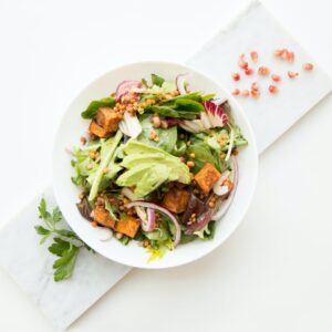 Platte auf der ein weißer Teller mit einem Salat mit Avocado und Lachs steht.