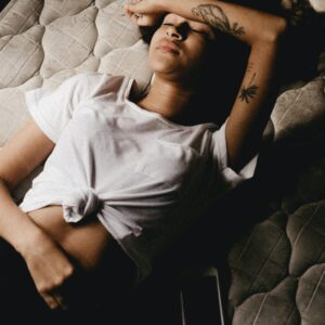 Frau liegt auf einem Bett mit geschlossenen Augen und hält sich ihren Bauch