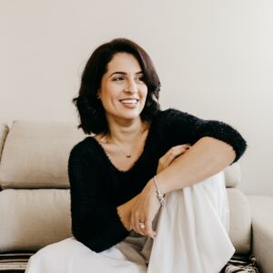 Frau mit braunen Haare sitzt auf beigem Sofa und lächelt