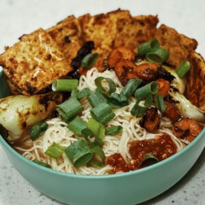 Bowl mit Tofu, Nudeln, Gemüse und Frühlingszwieblen auf einer Küchenplatte