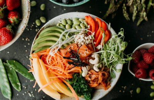 Bowl mit Avocado, Lachs und weiterem Gemüse auf einer dunklen Platte mit Obst