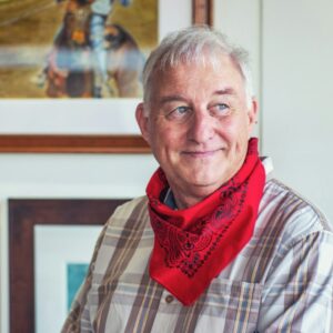 Älterer Mann im karierten Hemd mit roten Halstuch schaut zur Seite und lächelt.